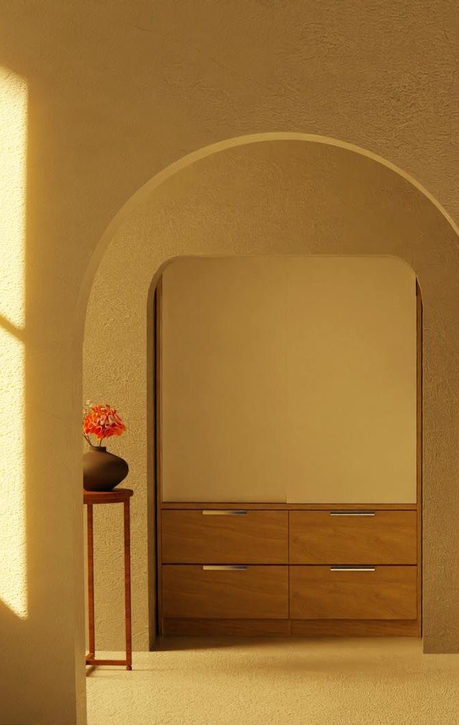 A warm sunlit room with an archway, wooden chair, and soft amber light casting shadows on plastered walls