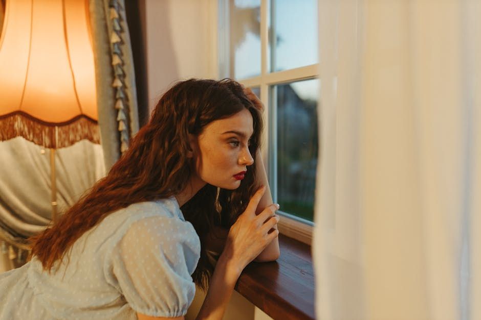 A young woman by a window, deciding whether to make the call