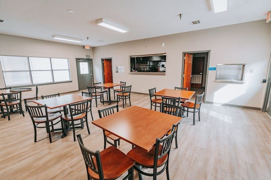 A dining room at Hickory Grove Recovery in Morrilton with square tables, chairs and a serving window into the kitchen