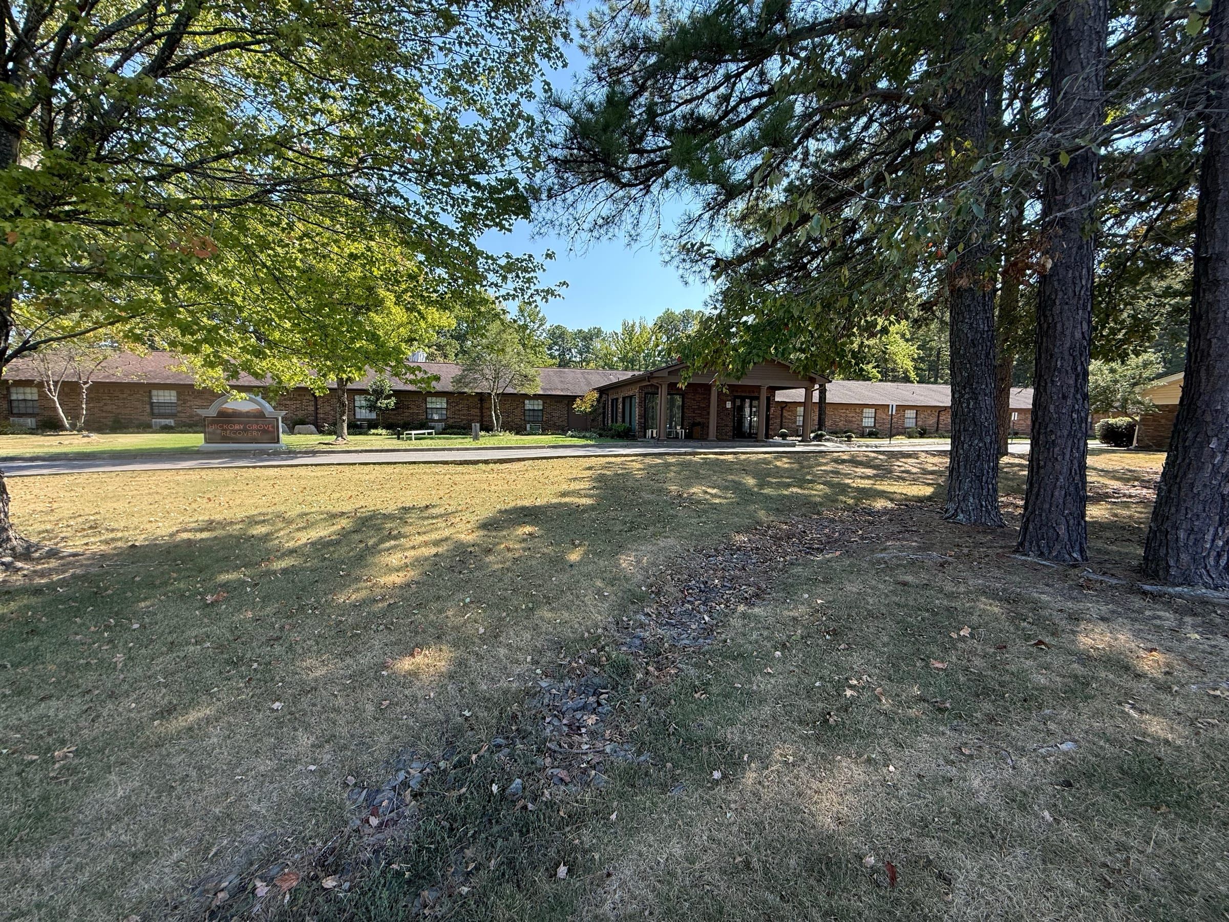 The front lawn at Hickory Grove Recovery in Morrilton, Arkansas, with tall pines and the brick building beyond.